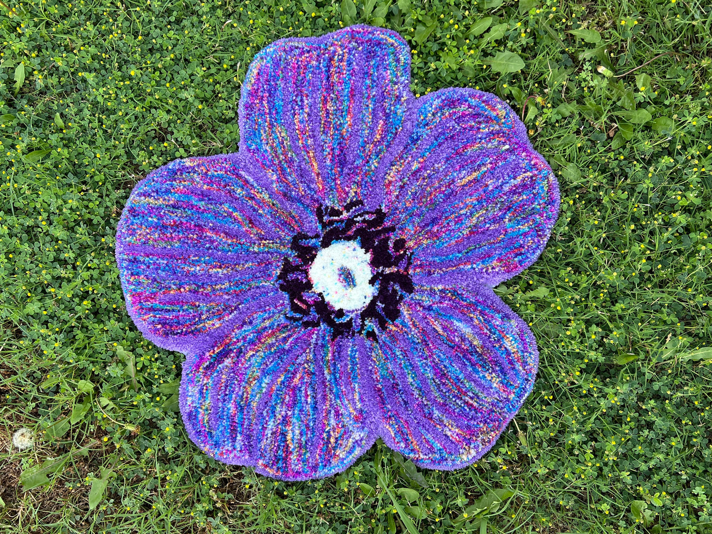 Purple flower-shaped rug on grass surface.