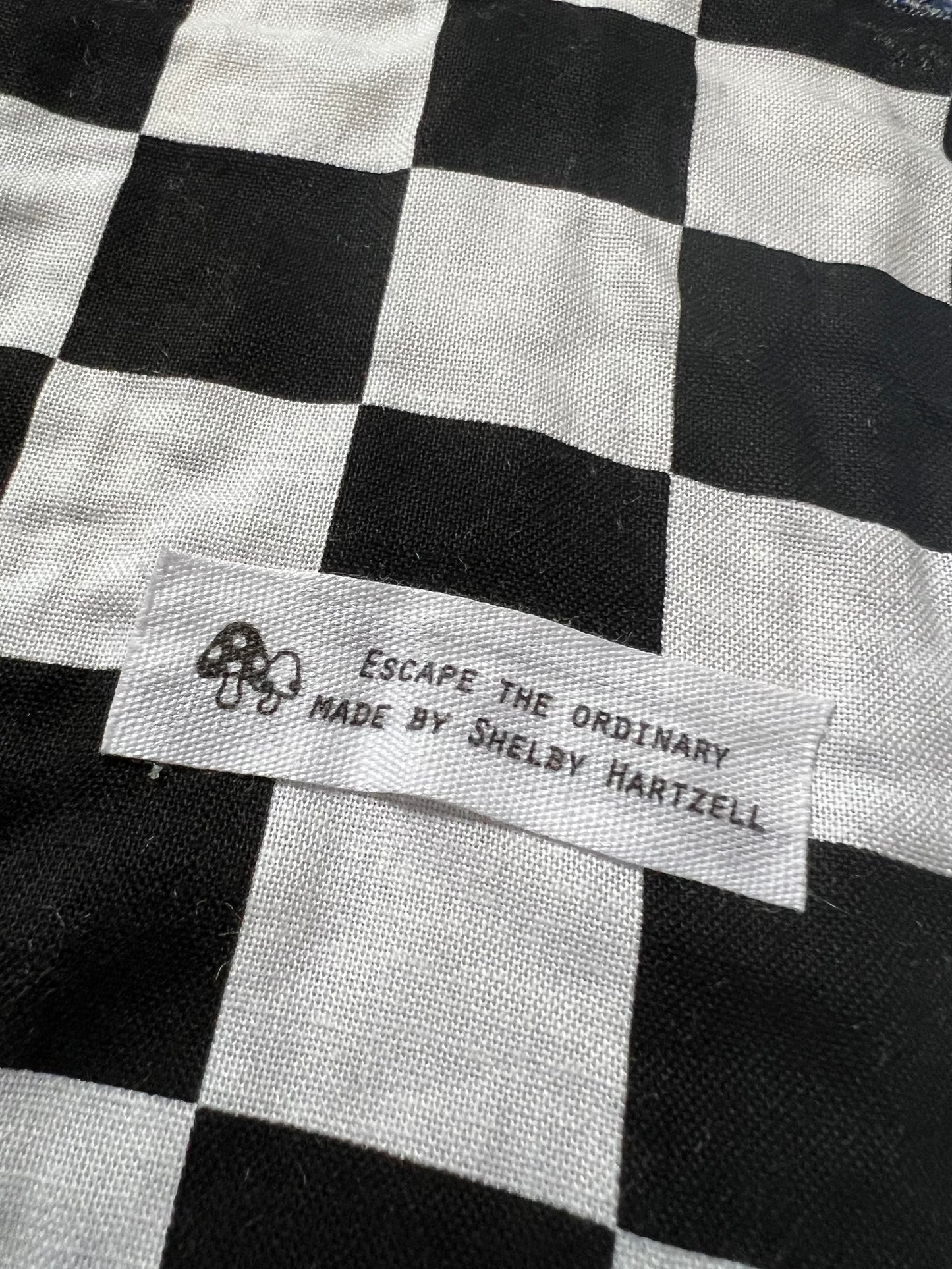 Checkered fabric with tag reading "Escape the Ordinary Made by Shelby Hartzell" for Blue Alien rug.
