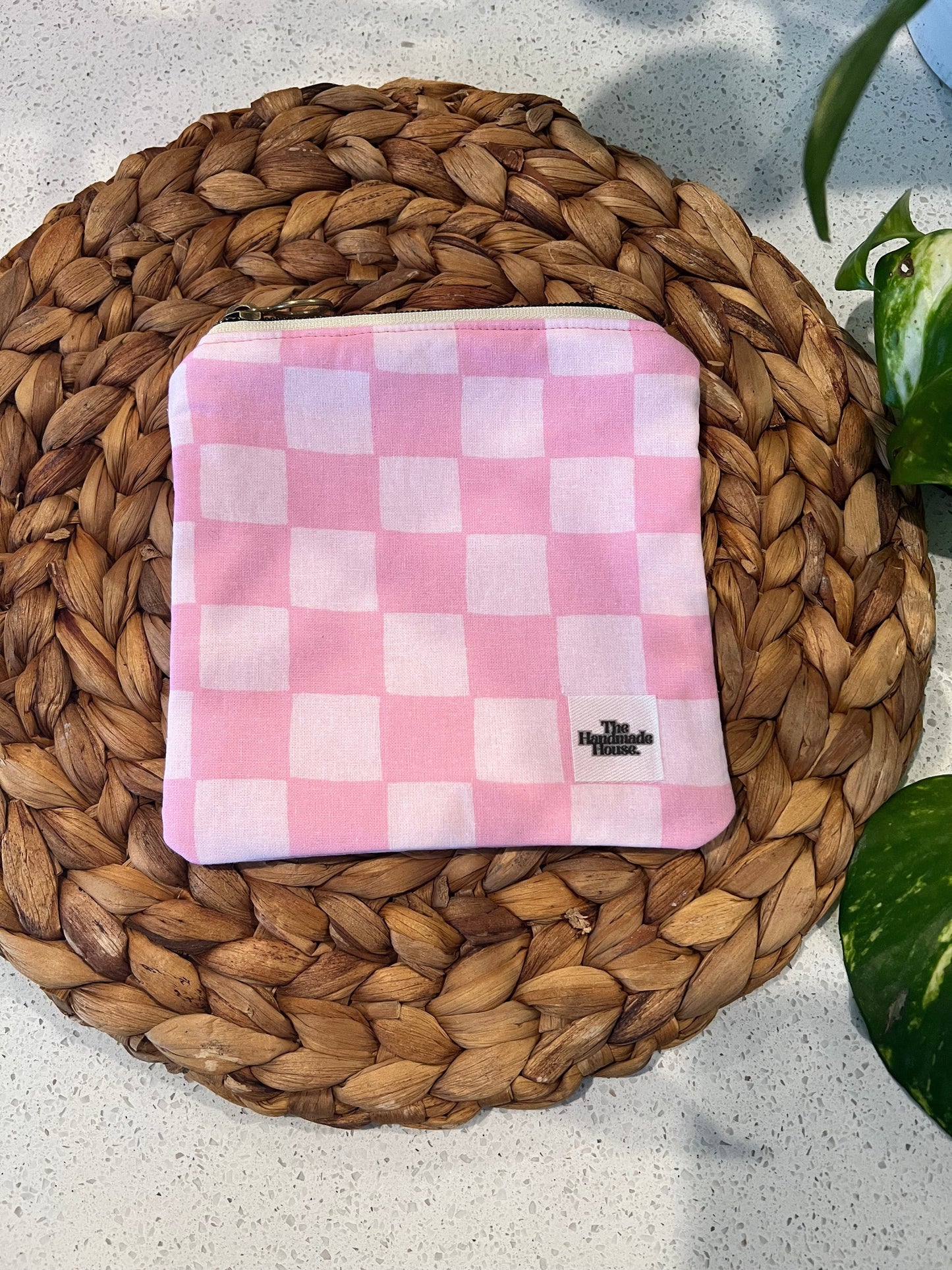 Pink checkered mini pouch on a woven mat surface.