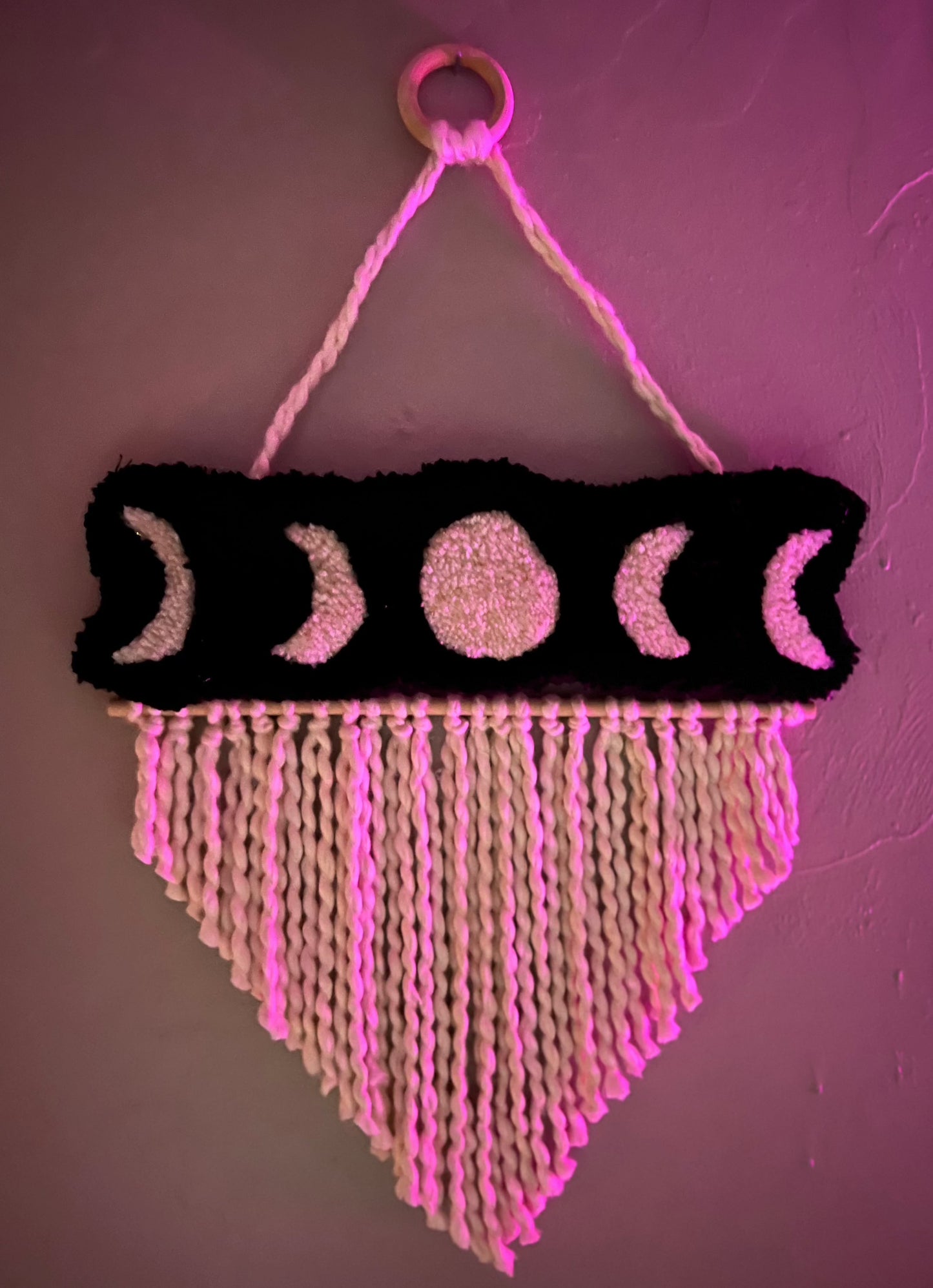 Moon phase wall hanging with black background and white braided fringe, size 21x13 inches.