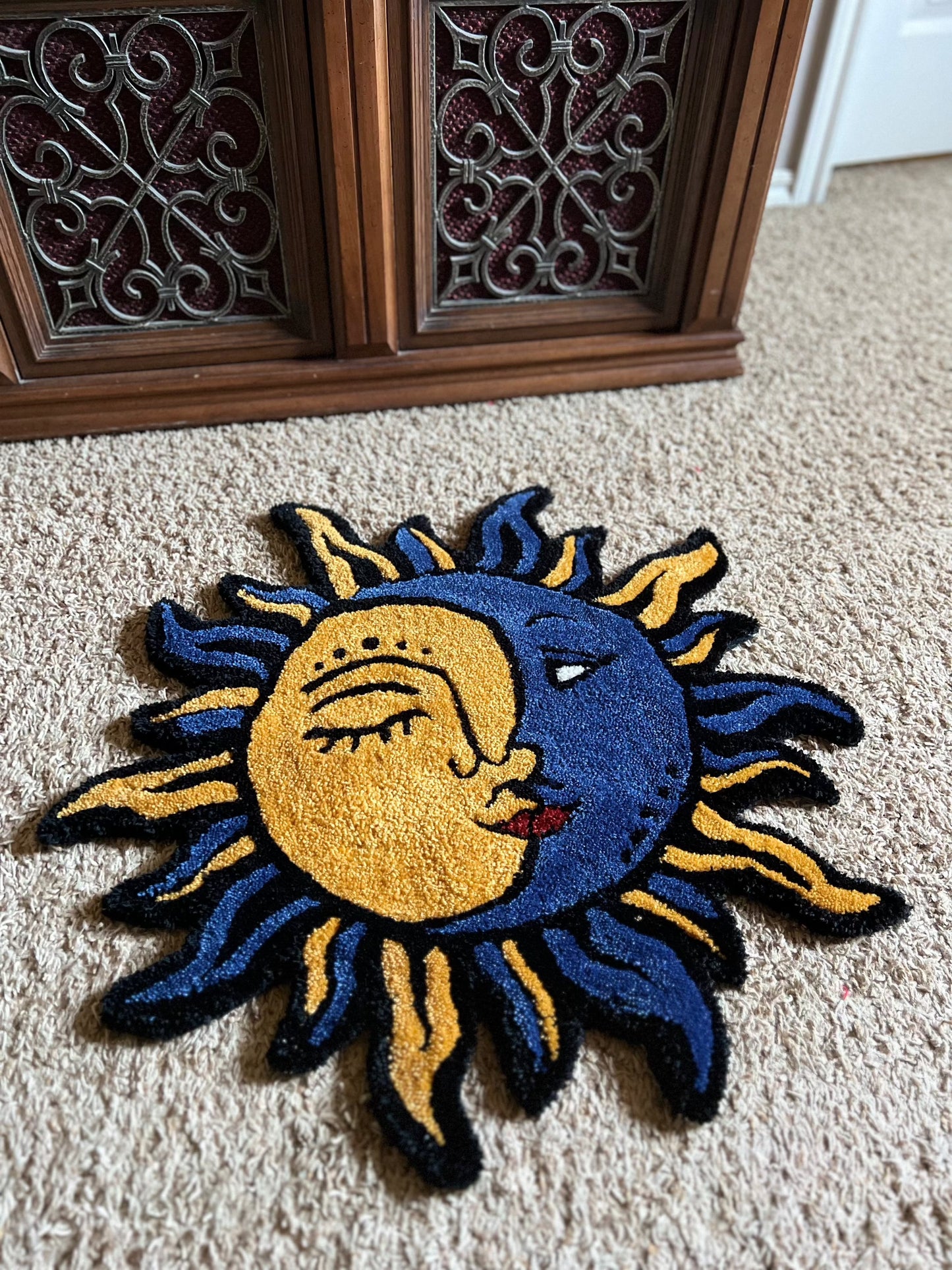 Round sun and moon-themed rug on beige carpet, 27 inches in size, with intricate blue and yellow design, titled "Drop 1: Sun-Moon".