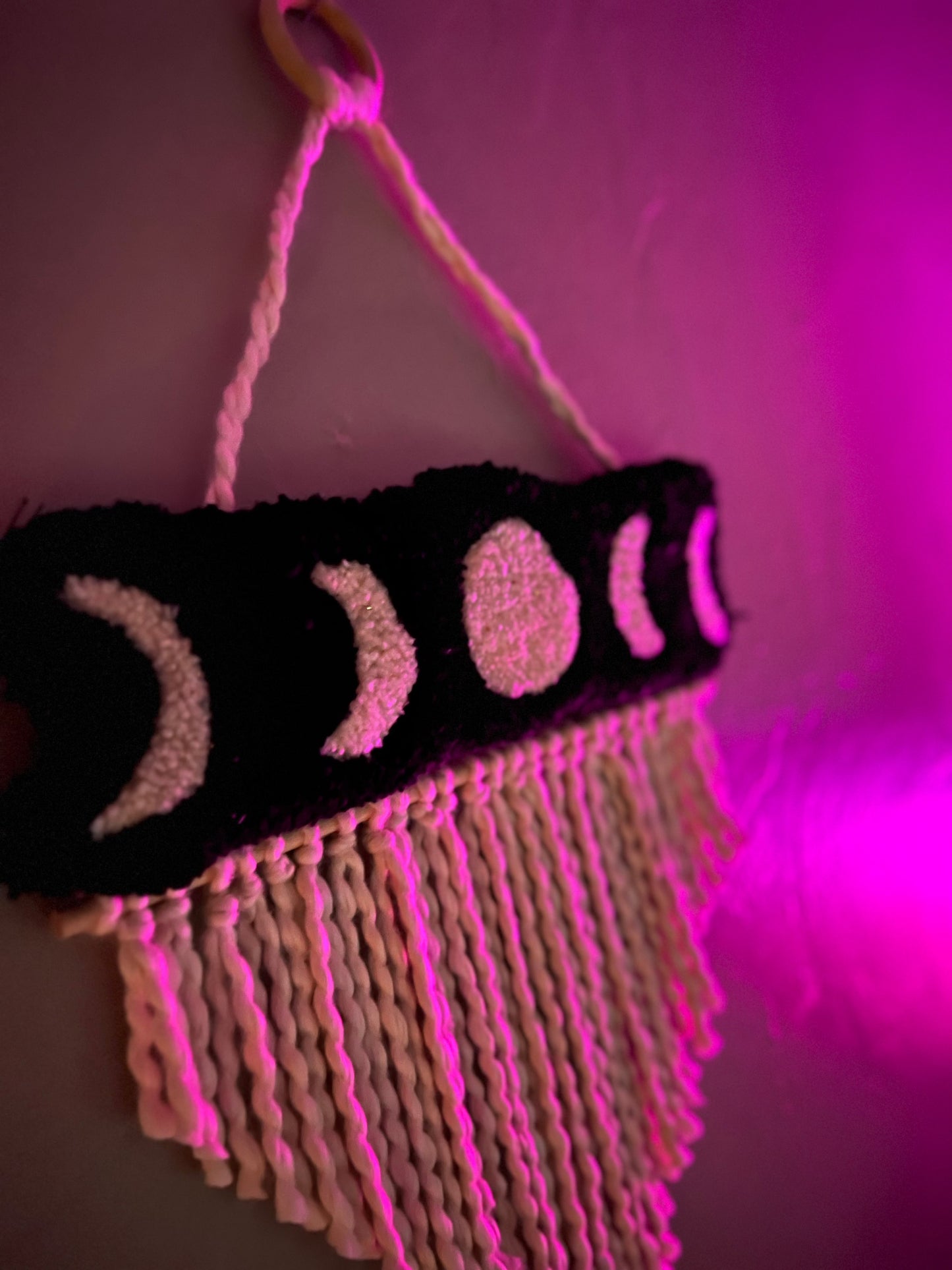 Moon phase wall hanging with fringes, size 21x13 inches, glowing under pink light.