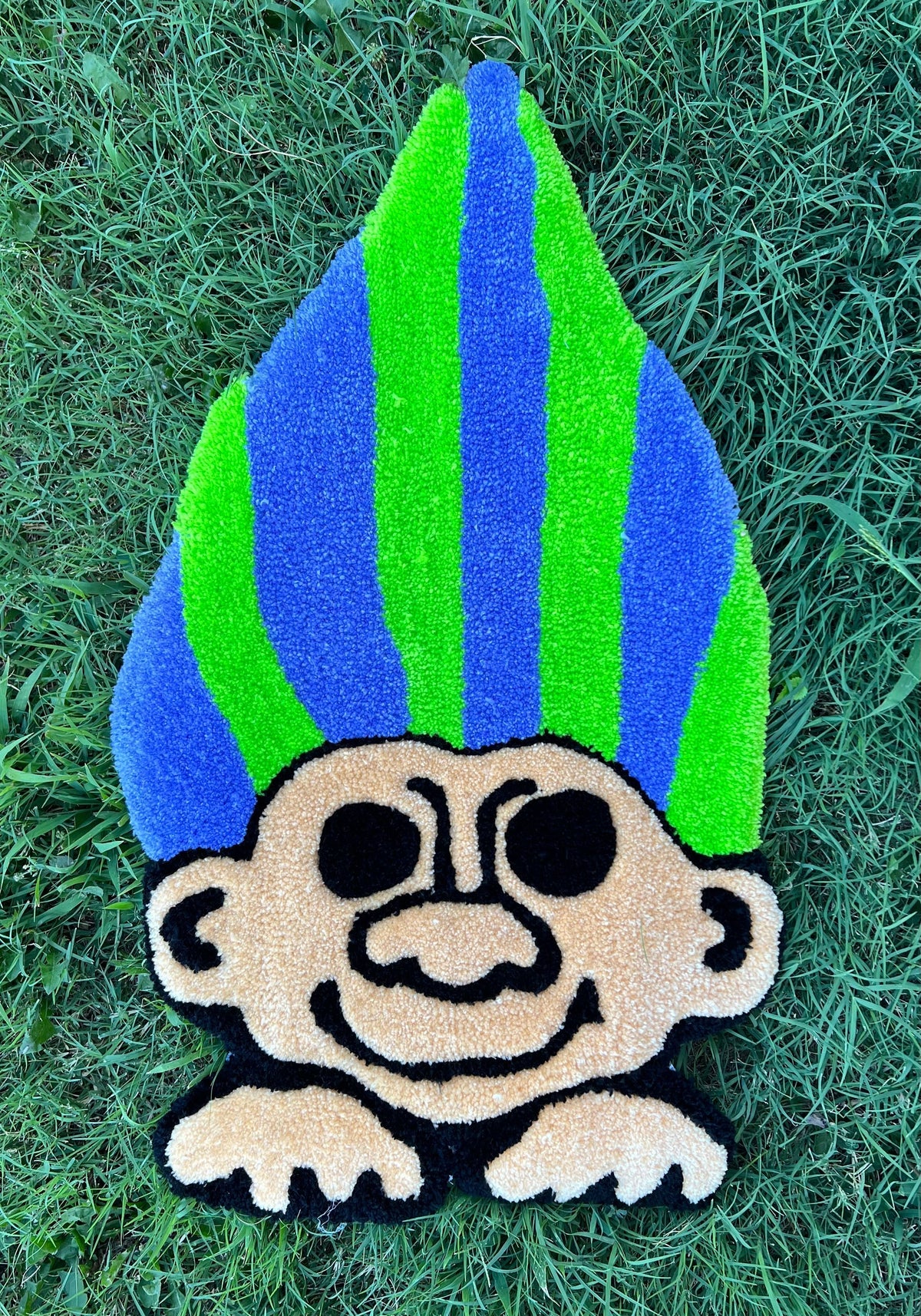 Neon Troll rug with vibrant green and blue hair on grass.