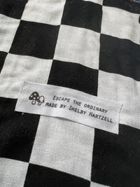 Checkered fabric with tag reading "Escape the Ordinary Made by Shelby Hartzell" for Blue Alien rug.