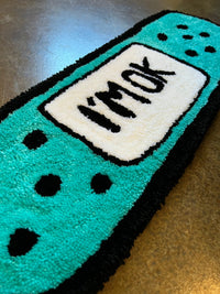 Teal and black rug shaped like a band-aid with "I'm okay" text.