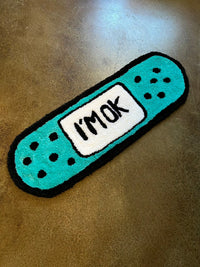 Drop 3 “I’m okay” Bandaid design rug on concrete floor.