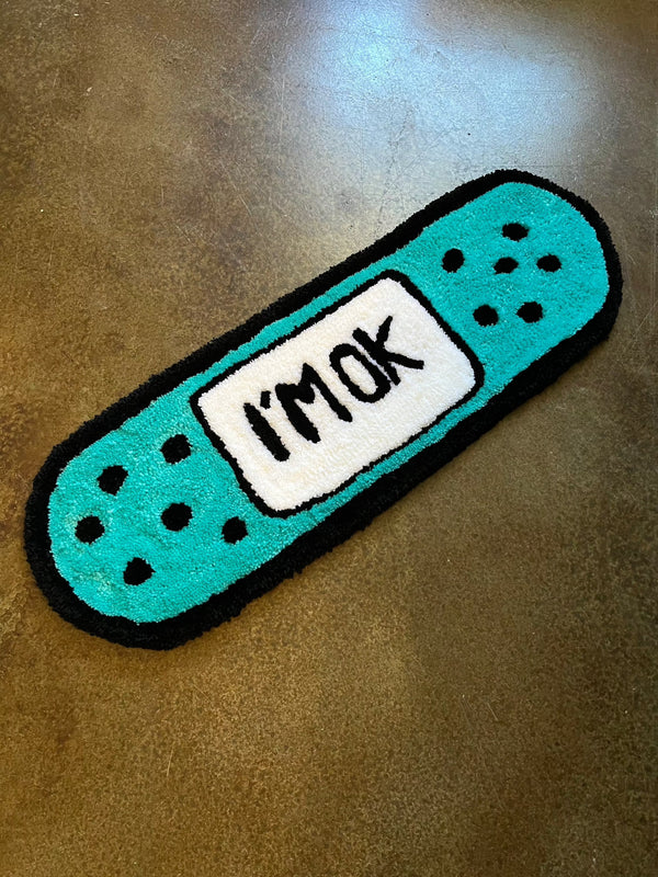 Drop 3 “I’m okay” Bandaid design rug on concrete floor.