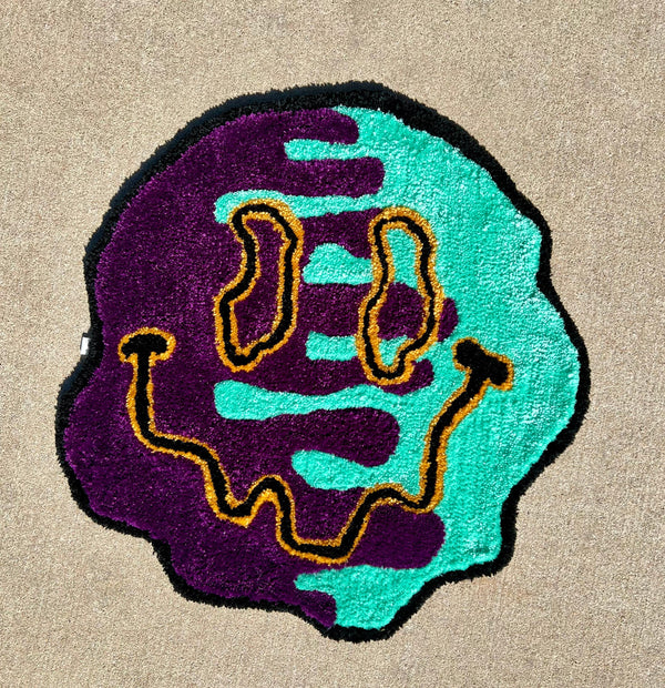Smiley face rug in black, dark yellow, teal, and dark purple, size 25x25 inches.