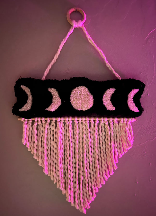 Moon phase wall hanging with black background and white braided fringe, size 21x13 inches.
